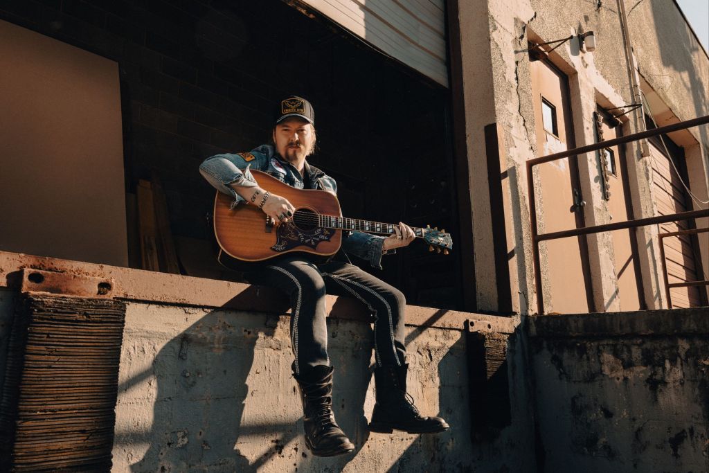 Drew Ryder Smith with an acoustic guitar at a weathered industrial loading dock, photographed by Julia Tabor.